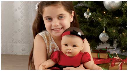 So Truly Mine doll photo gallery: a young girl holding her So Truly Mine baby doll while sitting beneath a Christmas tree